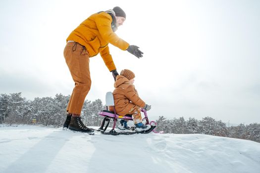 Father pulling little son on sledge in winter