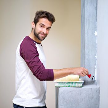 Making DIY look easy. Photo of an attractive young man painting a wall indoors.