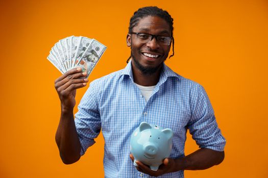 Portrait of amazed young man in casual shirt holding dollar banknotes against yellow background