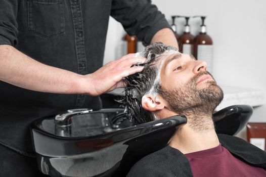 Barber shop. Hairdresser man washes client head in barbershop