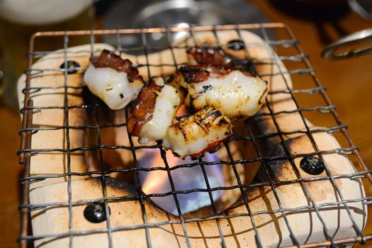 Selective focus of grilled octopus on charcoal stove. Food concept.