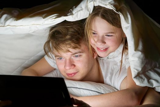 children play games on a tablet at night under a blanket, children watching video on tablet. communication through social networks.