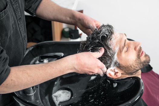 Barber shop. Hairdresser man washes client head in barbershop