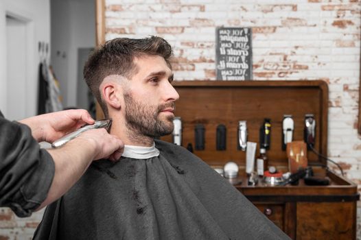 Man barber cutting hair of male client with clipper at barber shop. Hairstyling process.