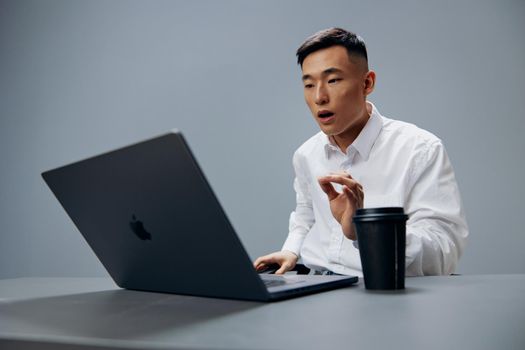 man in white shirts glass of coffee sits in front of a laptop office Gray background