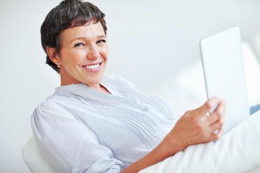 Smiling woman using digital tablet at home. Portrait of smiling mature woman using tablet PC while sitting on couch.