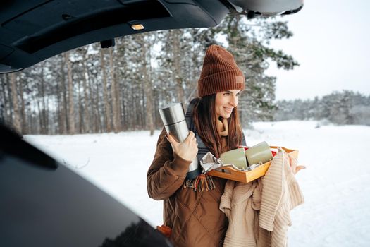 Young woman with hot drink thermos at winter forest