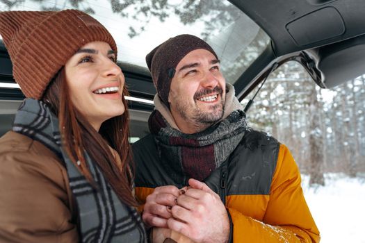 Lovely smiling couple sitting in car trunk in winter forest