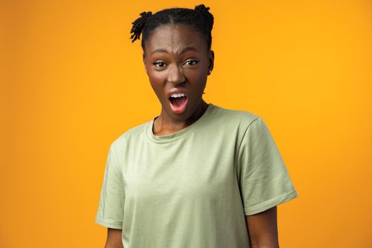 Frustrated beautiful African American female feels anxious and surprised, yellow studio