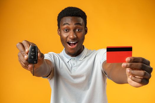 African man showing car key and credit card over yellow background