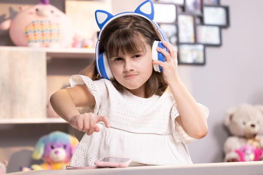 Small kid girl in headphones using funny editing application on smartphone, enjoying cool video or music content in social network, playing online games, communicating distantly