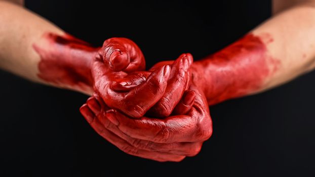 Woman holding blood-stained palms together on black background.