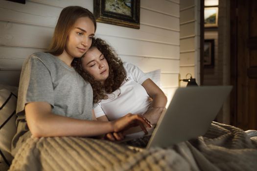 Two beautiful women lying in bed and watching movies on laptop