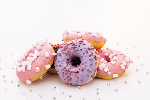 Assortment of donuts of different flavors. Chocolate frosted, pink glazed and sprinkles donuts. Donuts with different fillings on the white table
