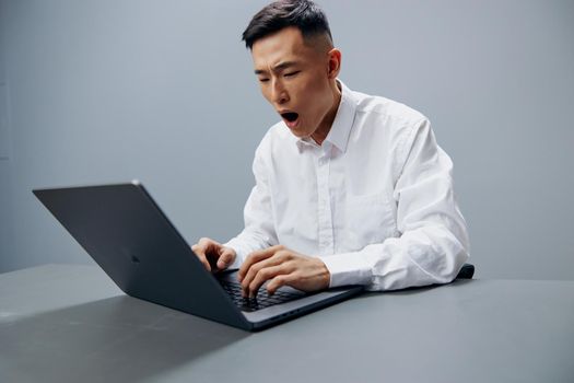 Asian man working on a laptop sitting at a table in the office Gray background