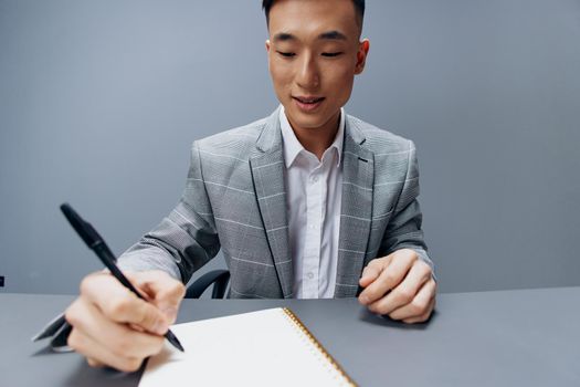 business man of Asian appearance in a gray suit writes on the table. High quality photo