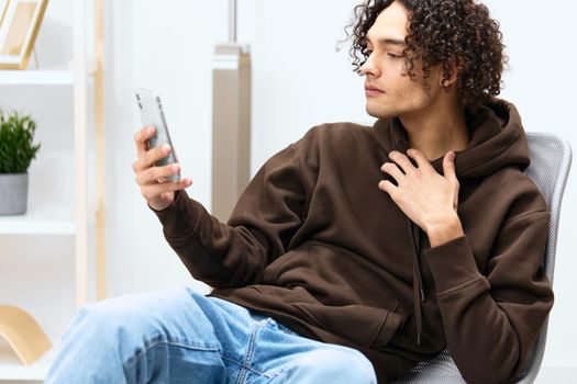 guy with curly hair sitting on a chair with a phone communication interior Lifestyle. High quality photo