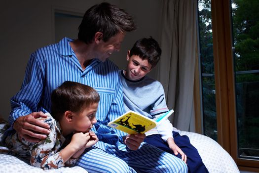 A tale before bedtime - Family Bonding. A father reading to his two sons at bedtime - Copyspace.