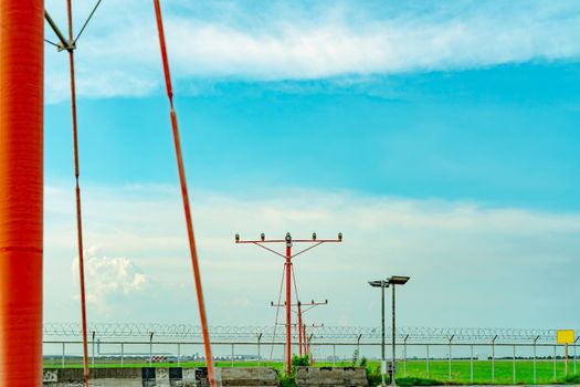 Approach light at the airport. Approach light system concept. Airport runway approach lights. ALS of the airport. Fence for security. Landscape of the airport with green grass field and blue sky.