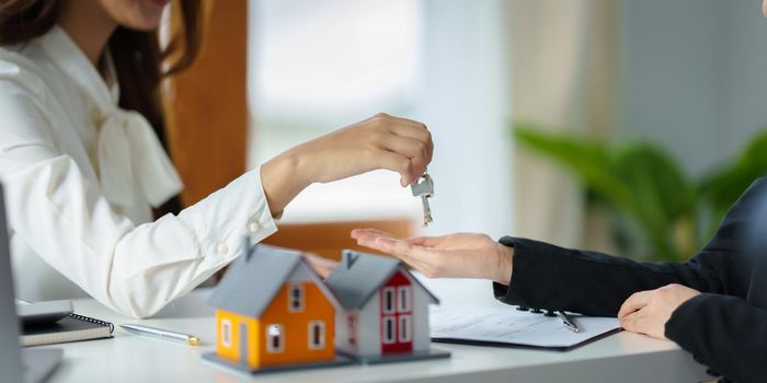 The real estate agent or agency giving house key to customer after signing agreement contract. Property concept.