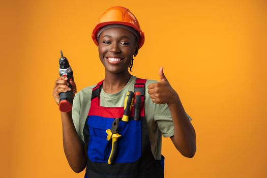 Smiling young african american woman in hardhat holding screwdriver tool in studio