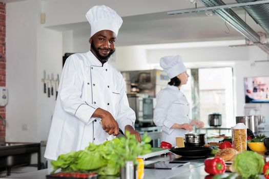 Confident head chef in restaurant professional kitchen, cutting vegetables and preparing garnish for dinner dish recipe.