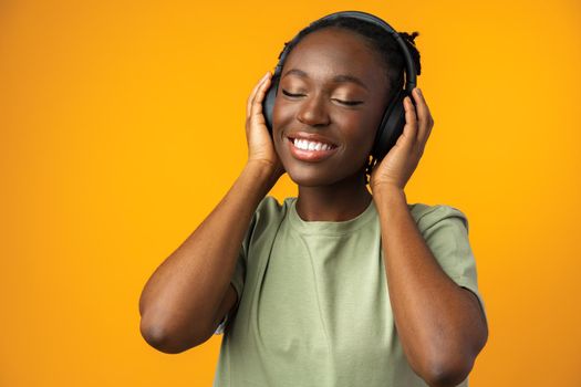 Happy young Afro American woman listening to music in headphones against yellow background