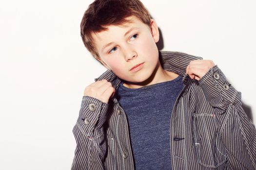 Hes got his own personal style. Young adolescent boy adjusting his shirt against a white background.