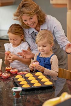Making yummy sweet treats. A grandmother and her two grandchildren decorating cupcakes at home.