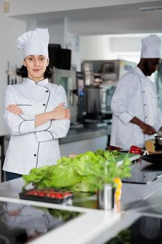 Food industry worker standing in restaurant kitchen with arms crossed after vegetable cutting.