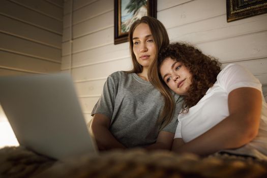 Two beautiful women lying in bed and watching movies on laptop