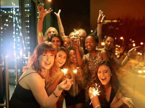 Sparkling into the New Year. Shot of a group of girlfriends having fun with sparklers on a balcony on a night out.