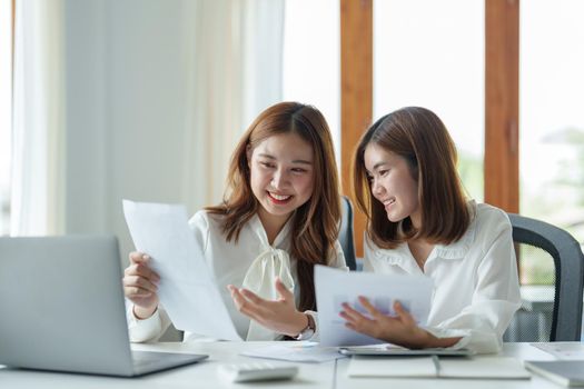 Two colleagues or students, asian girl working for financial paperwork while sitting at workplace discussing about job or education.