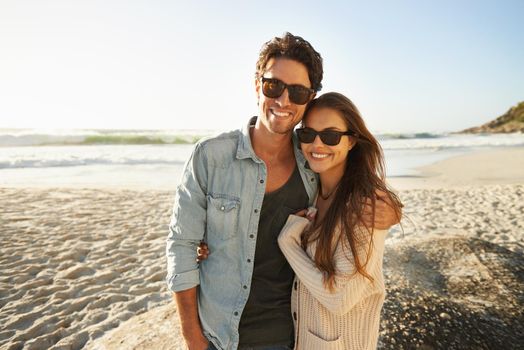 Enjoying the sea breeze and sun. Shot of a beautiful young couple standing side by side on the beach.