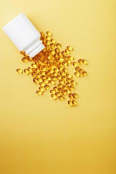 Golden Omega-3 fish oil capsules poured out of a jar on a yellow background