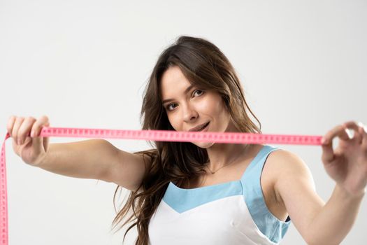 Attractive sexy brunette woman with slim body looking in a camera and showing a pink centimeter tape. Healthy lifestyles concept. Sport and diet.