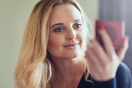 Looking good and feeling great. Shot of an attractive young woman looking at her face in a compact mirror.