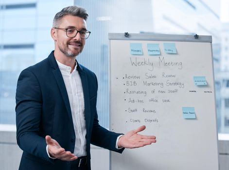 Welcome all to our weekly meeting. Shot of a mature businessman using a whiteboard during a presentation in an office.