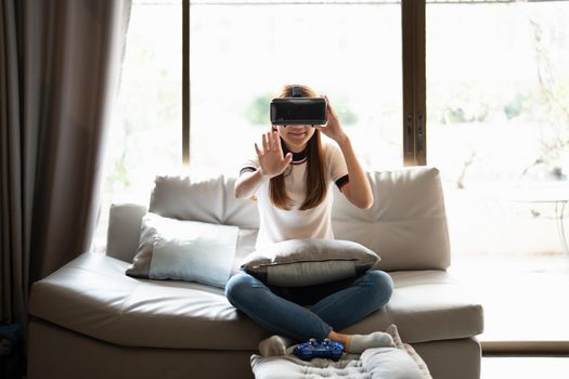 Concept of technology,gaming,entertainment and people.asian woman enjoying virtual reality glasses while relaxing in living room.Happy young guy with VR headset playing video game at home