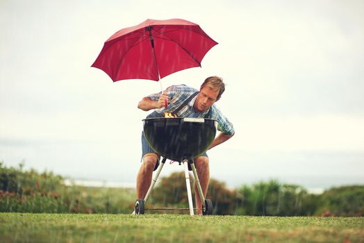 The rain wont stop my barbecue. Shot of a man trying to barbeque in the rain.