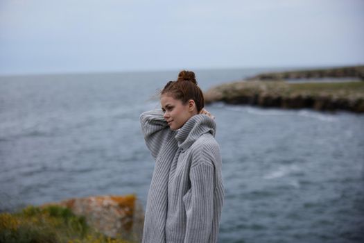 woman in a gray sweater stands on a rocky shore nature Lifestyle