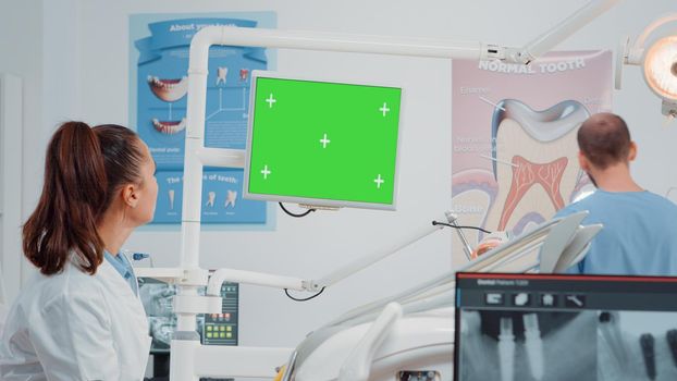 Dental team working with green screen on computer in cabinet for oral care. Dentist and assistant talking while looking at isolated background and mockup template for dentistry.