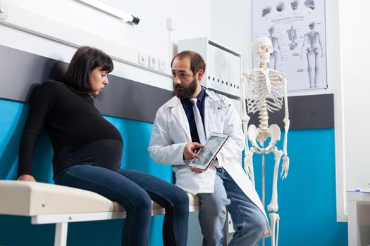 Obstetrician showing human skeleton on digital tablet to patient