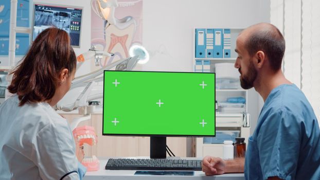 Dentist and man nurse analyzing green screen on computer while looking at teeth scan for oral care in dental office. Dentistry specialists using isolated background and mockup template