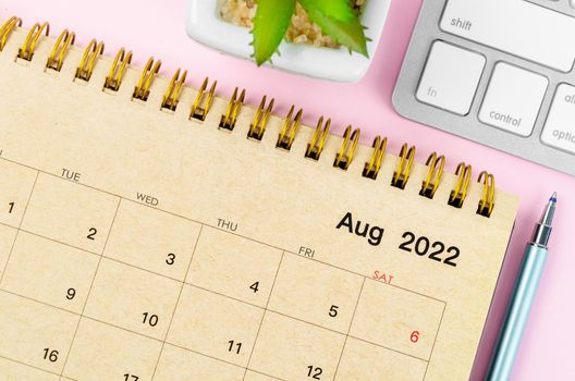 August 2022 desk calendar with keyboard computer on pink background.