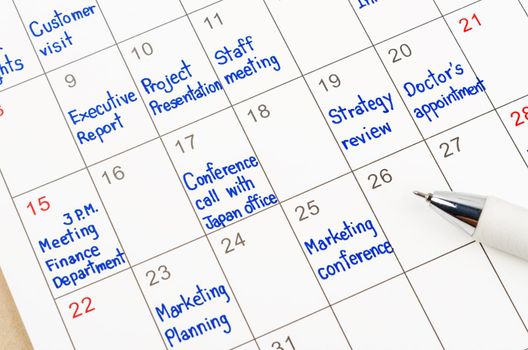 Handwriting scheduling appointments on calendar sheet with pen.
