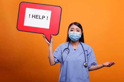 Healthcare clinic scared nurse wearing stethoscope and medical clothing asking for help. Hospital caregiver holding cardboard speech bubble sign while wearing stethoscope and medical uniform.