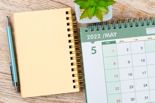 May 2022 desk calendar and diary with small plant on wooden background.
