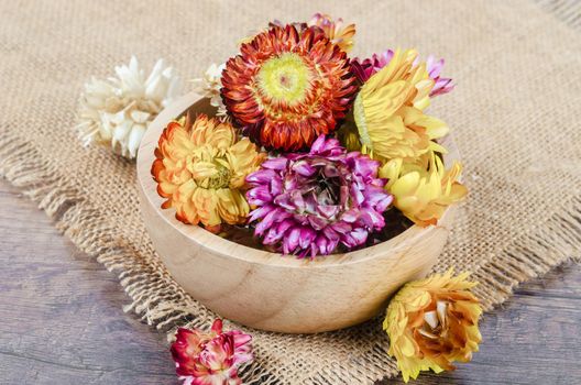 Dried straw flower heads in wooden cup on wooden background.