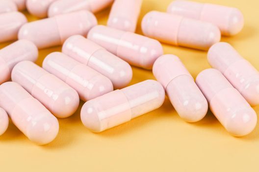 Pink capsule pills on yellow background 